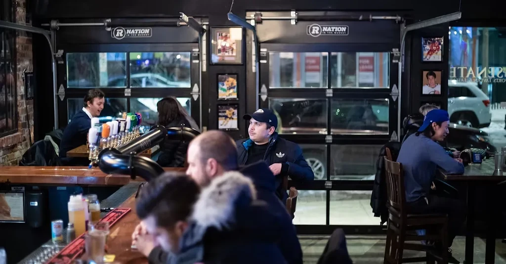 Dimly lit pub with patrons, staff, sports memorabilia, and 'R Nation' logos.