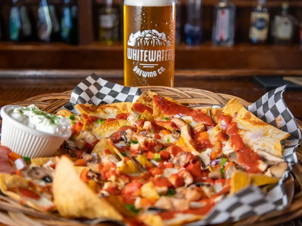 Nachos with cheese, vegetables, chicken, dip, and a beer.