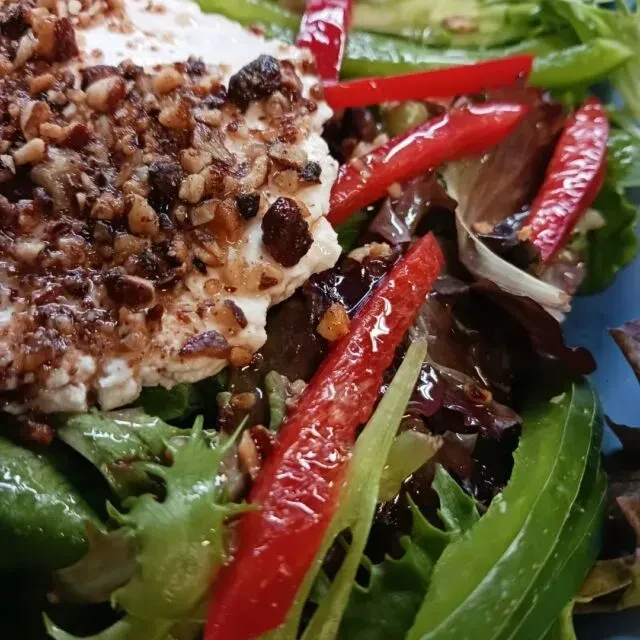 Salad with white cheese, nuts, dried fruit, leafy greens, and red bell pepper.