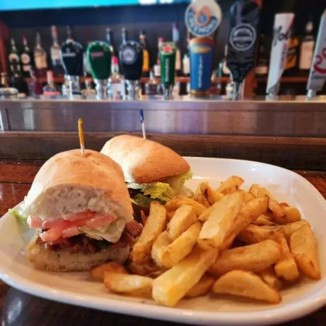 Plated sandwich and fries with a blurred bar background.