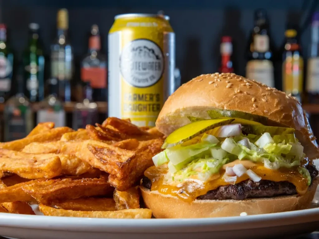 Loaded cheeseburger, golden fries, and beer can on a white plate.