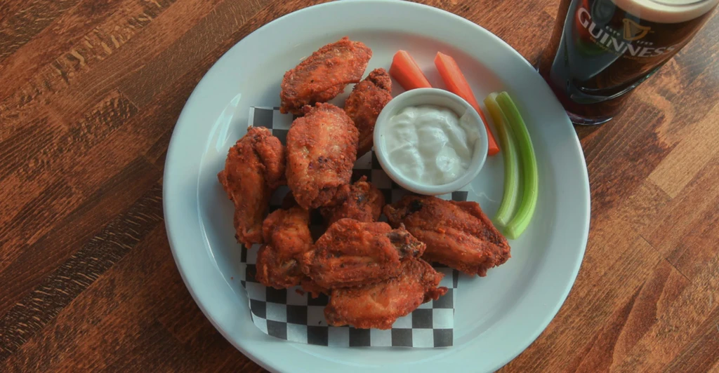 Plate of crispy chicken wings, vegetables, dipping sauce, and Guinness.