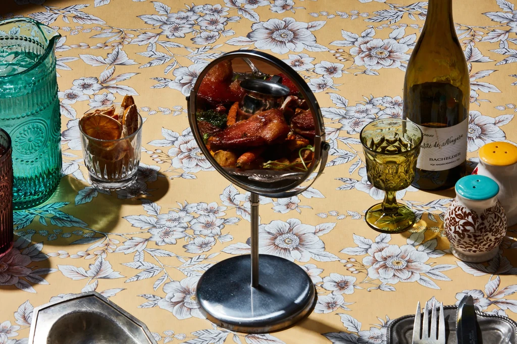 Warmly lit dining table features a reflected roasted meal and wine.
