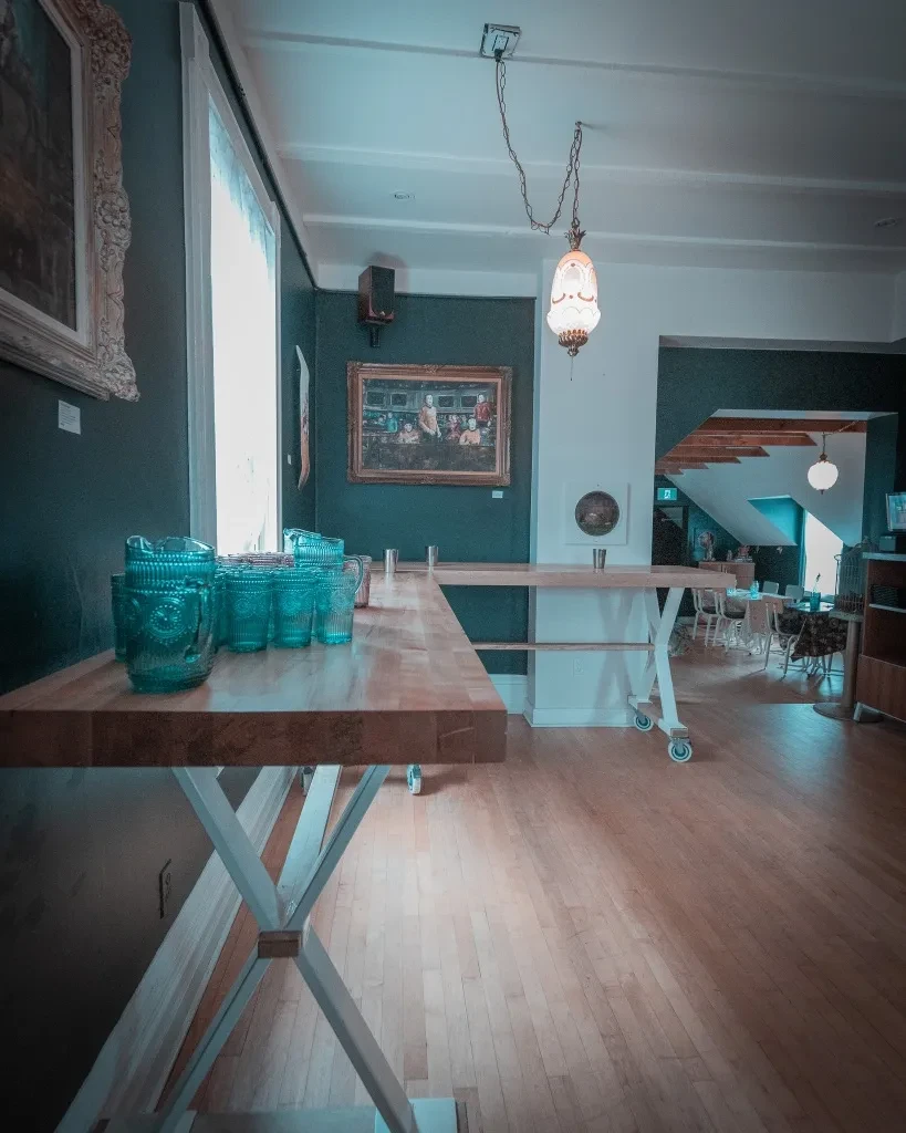 Restaurant interior with long wooden tables, turquoise pitchers, and framed artwork.