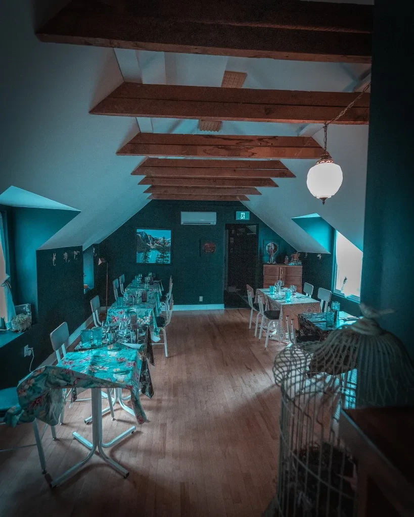Empty dining room with sloped wooden ceiling, exposed beams, and set tables.