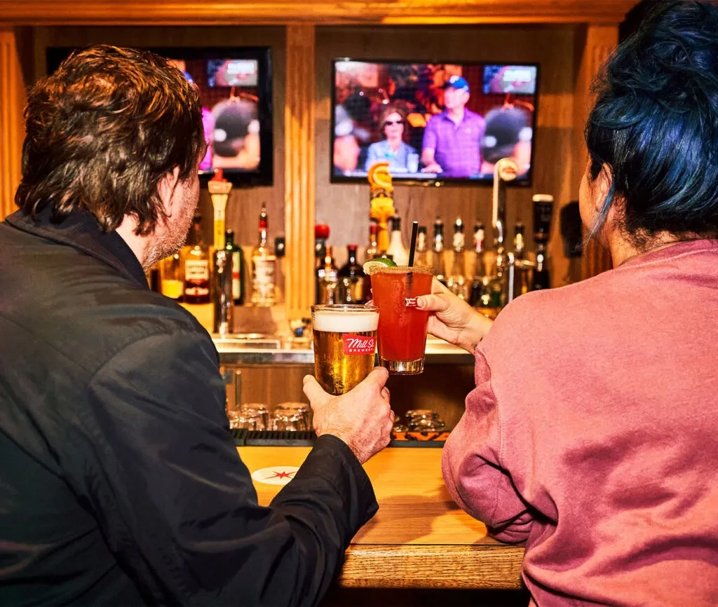 Man with beer, woman with cocktail, sitting at a bar.