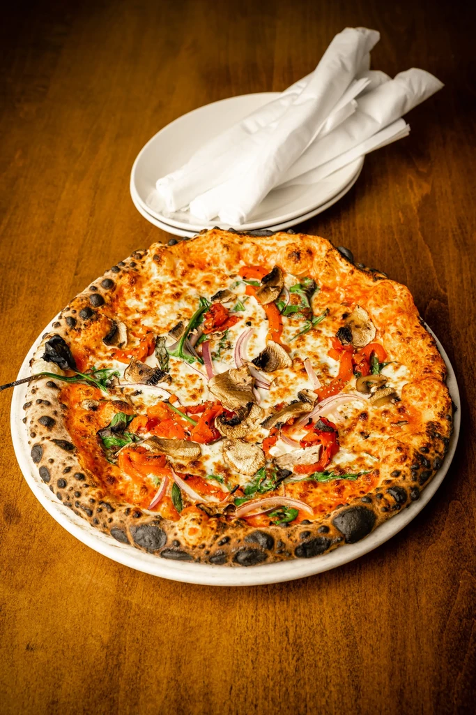 Charred crust pizza with melted cheese and fresh vegetables.