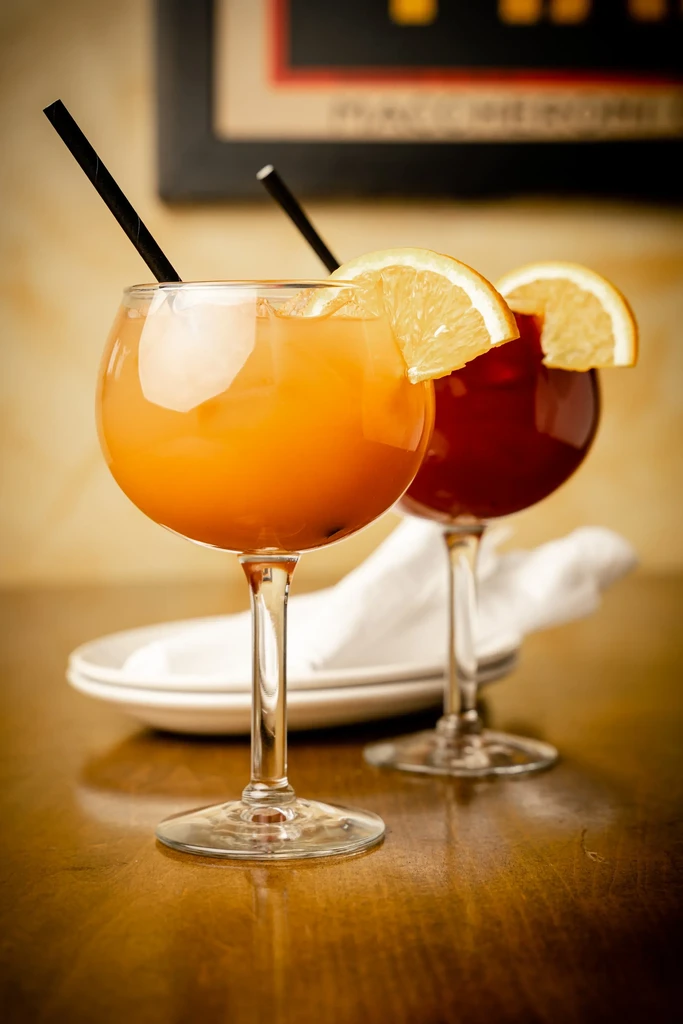 Orange and red cocktails in stemmed glasses on a wooden table.