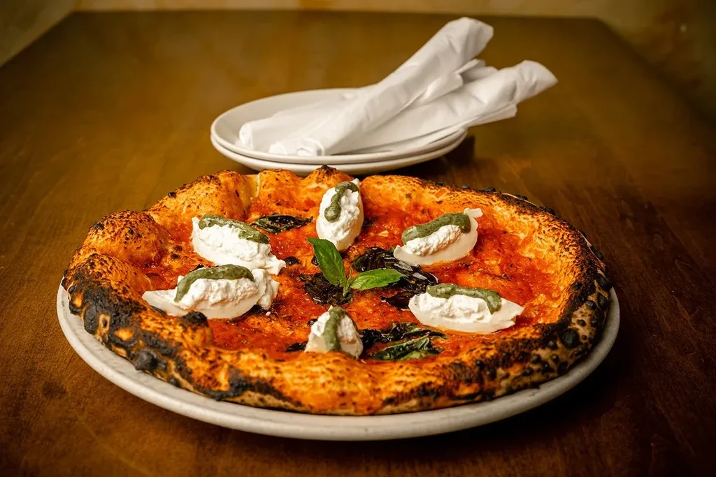 Neapolitan pizza with charred crust, tomato sauce, white cheese, and pesto.