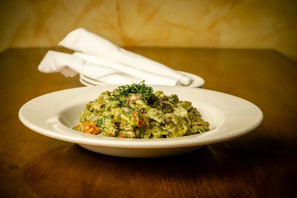 Close-up of pasta with green sauce, grated cheese, and herbs.