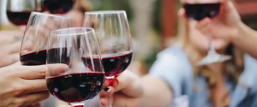 Close-up of hands raising multiple red wine glasses in a toast.