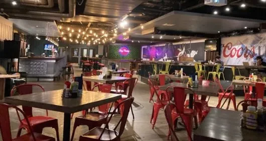 Warm industrial-chic bar interior with red chairs, yellow stools, and murals.