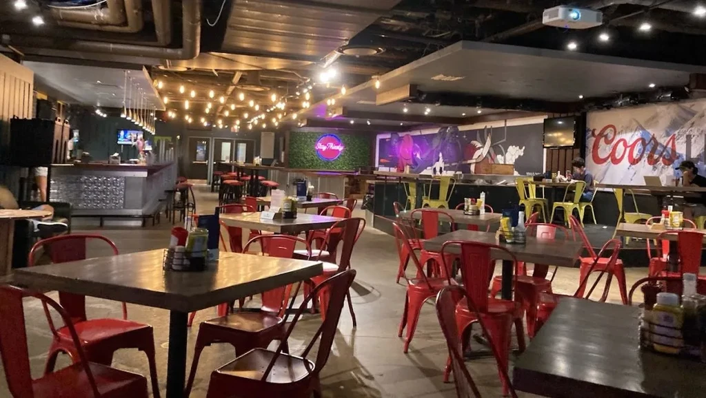 Cozy bar interior with industrial ceiling, colorful seating, and neon art.