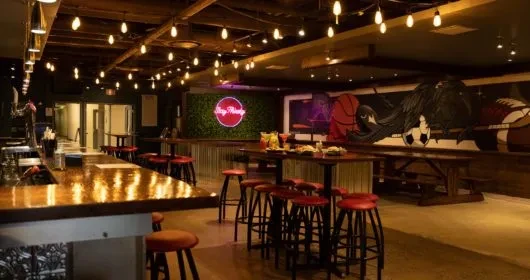 Vibrant, modern sports bar with 'Sip N Play' neon sign and sports mural.