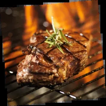Thick grilled steak with rosemary on a metal grill over flames.