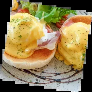 Close-up of two Eggs Benedict halves with hollandaise, herbs, and side salad.