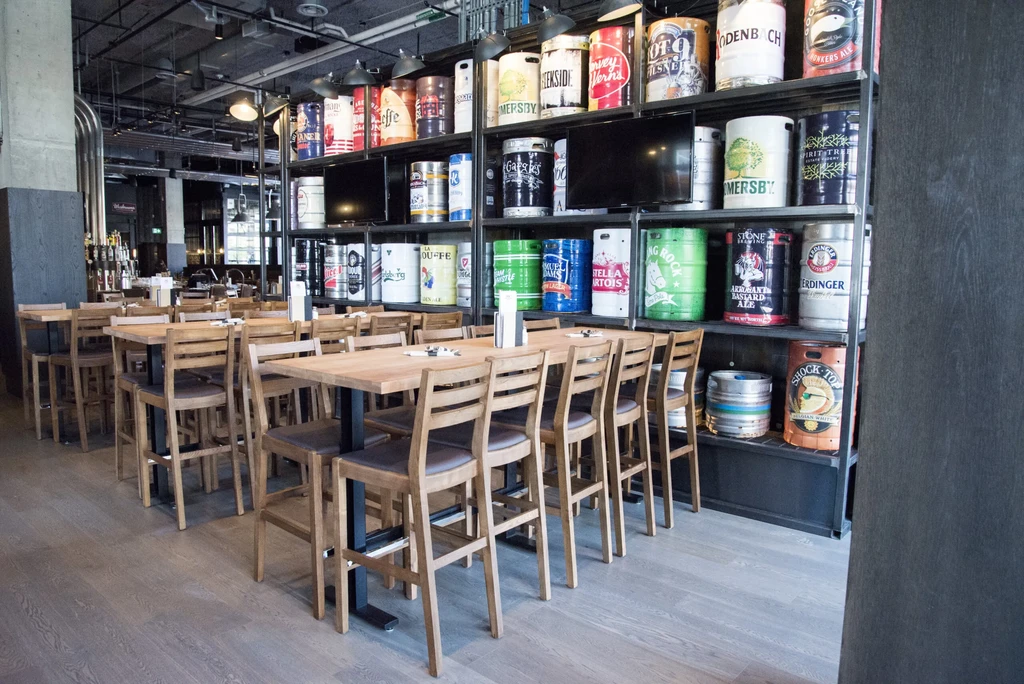 Modern restaurant with wooden tables and colorful beer keg wall.
