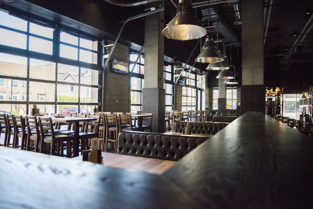 Empty modern restaurant with industrial-chic design, large windows, and varied seating.