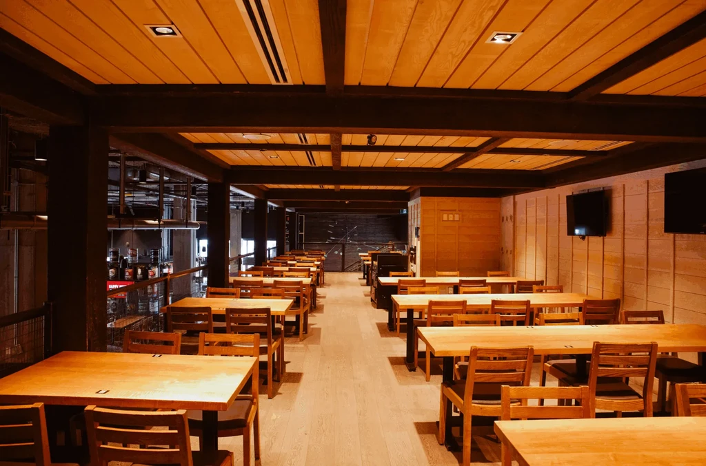 Empty restaurant: rustic wooden tables, industrial style, wall-mounted TVs.
