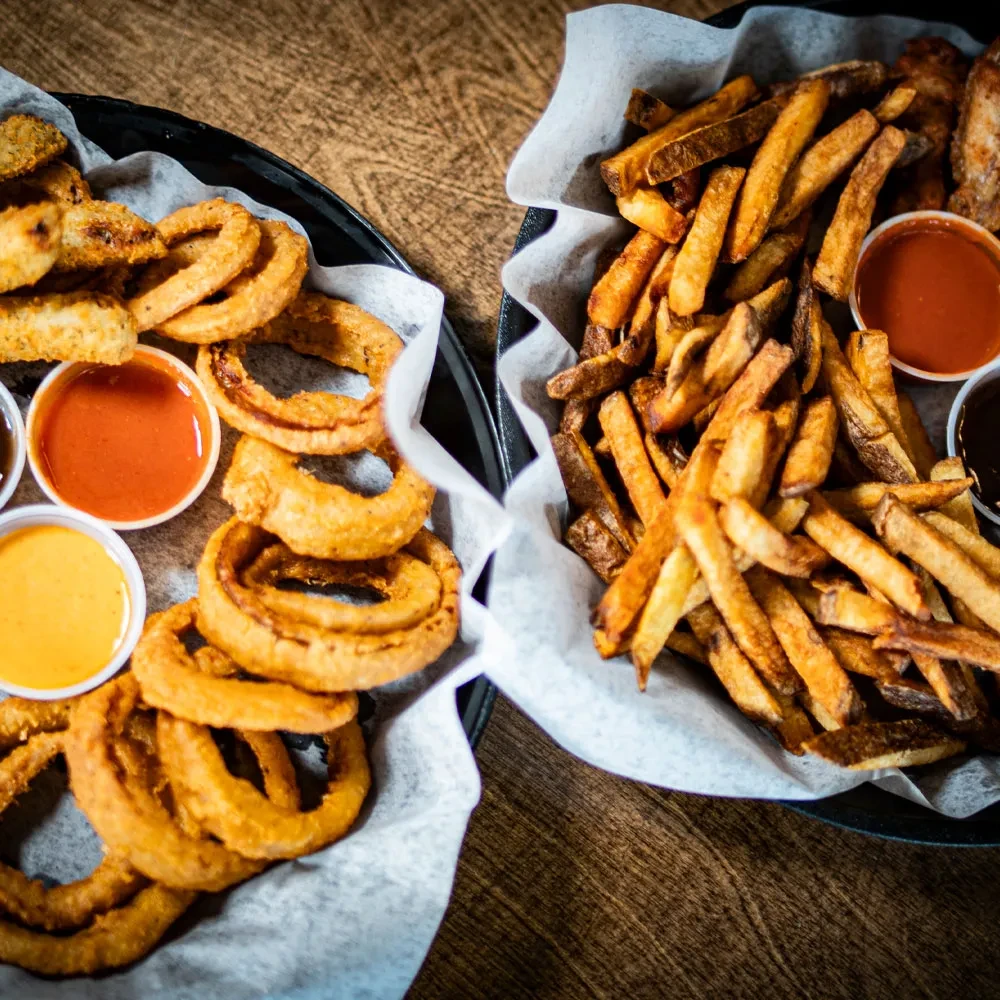 Baskets of golden onion rings, French fries, chicken wings, and sauces.