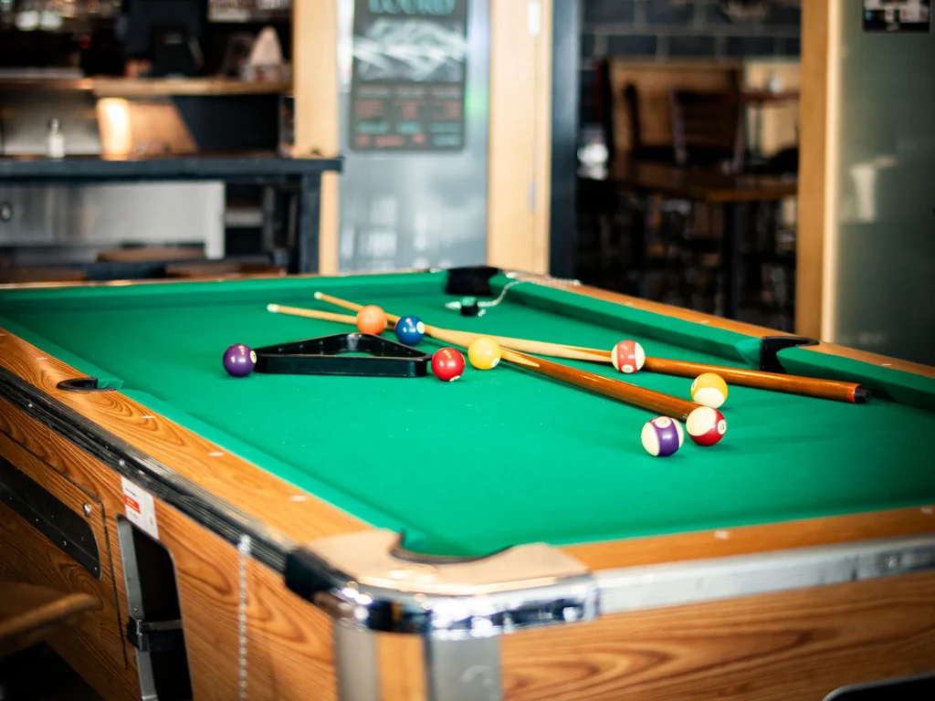 Vibrant green pool table with balls, cues, and rack in a bar.