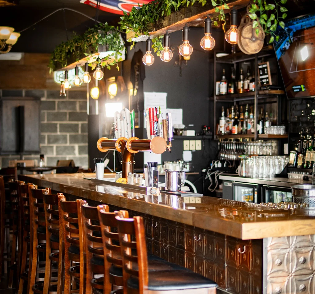 Rustic industrial bar with polished wood counter, beer taps, and warm lighting.