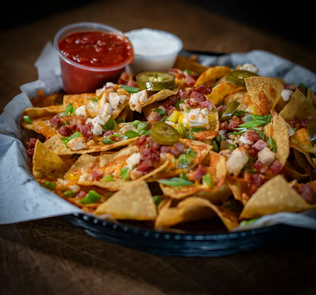 Loaded nachos in basket with cheese, chicken, bacon, jalapeños, sauces.