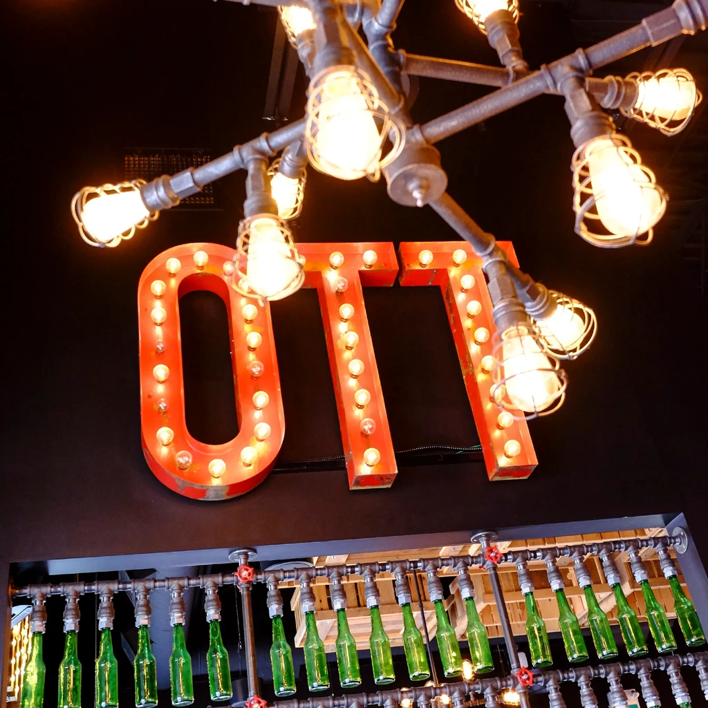 Industrial pipe chandelier above 'OTT' marquee letters and bottle fixture.