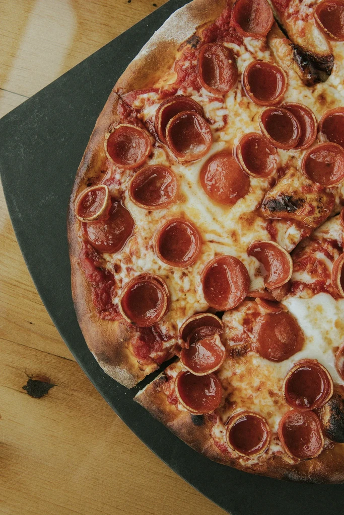 Overhead pepperoni pizza with bubbly cheese, curled pepperoni, and a cut slice.