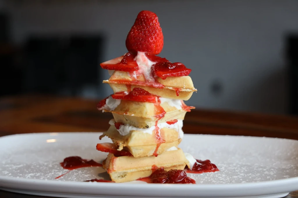 Stack of waffles with whipped cream, fresh strawberries, and strawberry sauce.