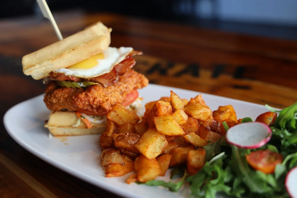 Savory waffle sandwich with fried chicken, bacon, egg, potatoes, and salad.