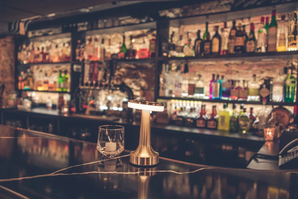 Atmospheric bar interior: candle, modern lamp, blurred glowing bottles.
