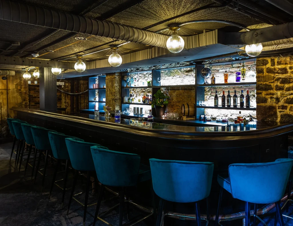 Dark, curved bar with teal stools and backlit liquor bottle display.