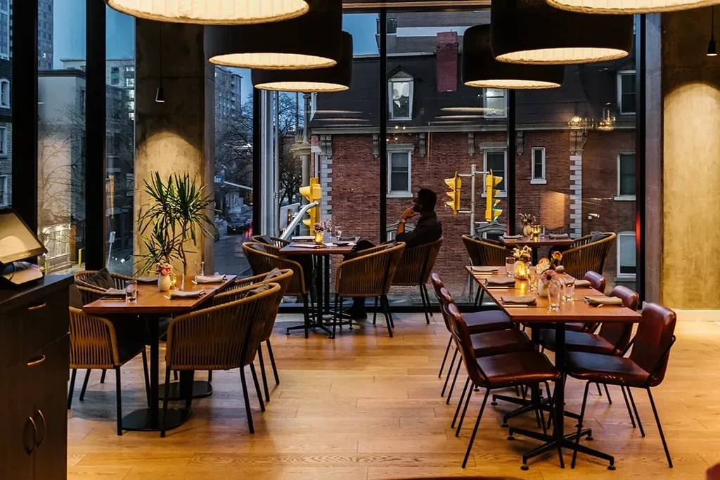 Warmly lit modern restaurant with tables, city view, and one person.