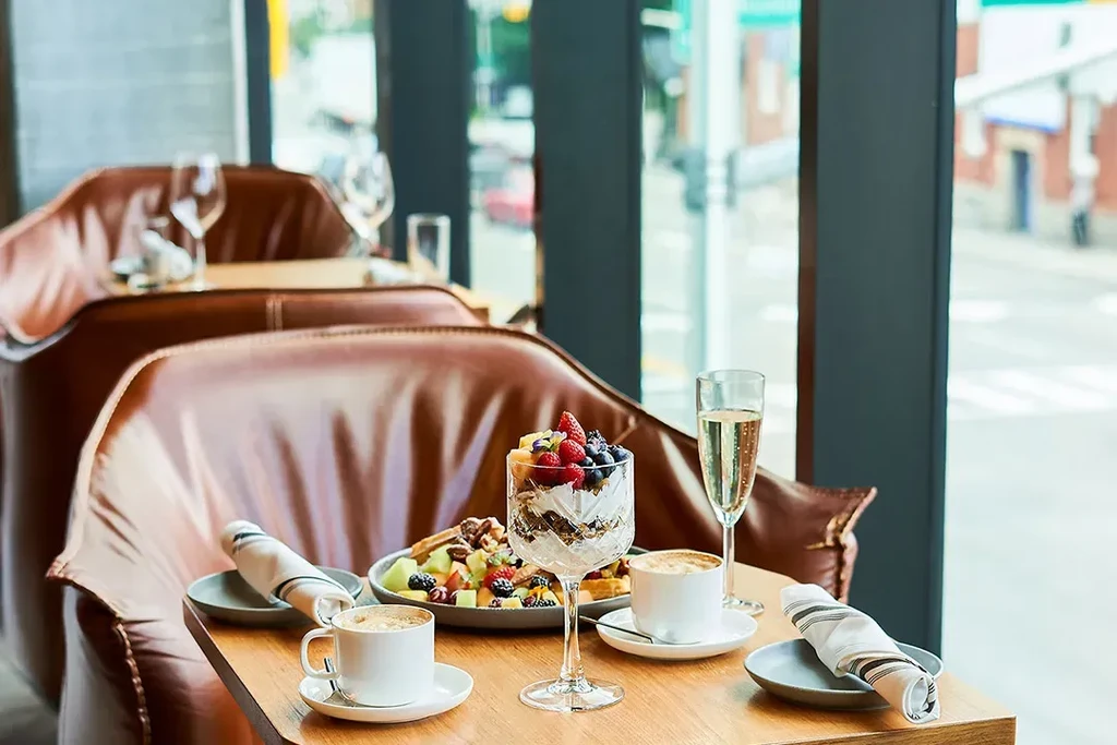 Restaurant table with parfait, waffles, coffee, and sparkling drink, urban view.
