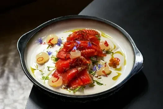 Plated red-orange cured fish with microgreens, flowers, and green oil.
