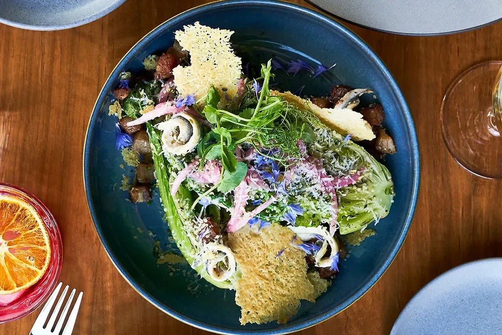 Vibrant salad in a dark blue bowl with lettuce, cheese, and flowers.