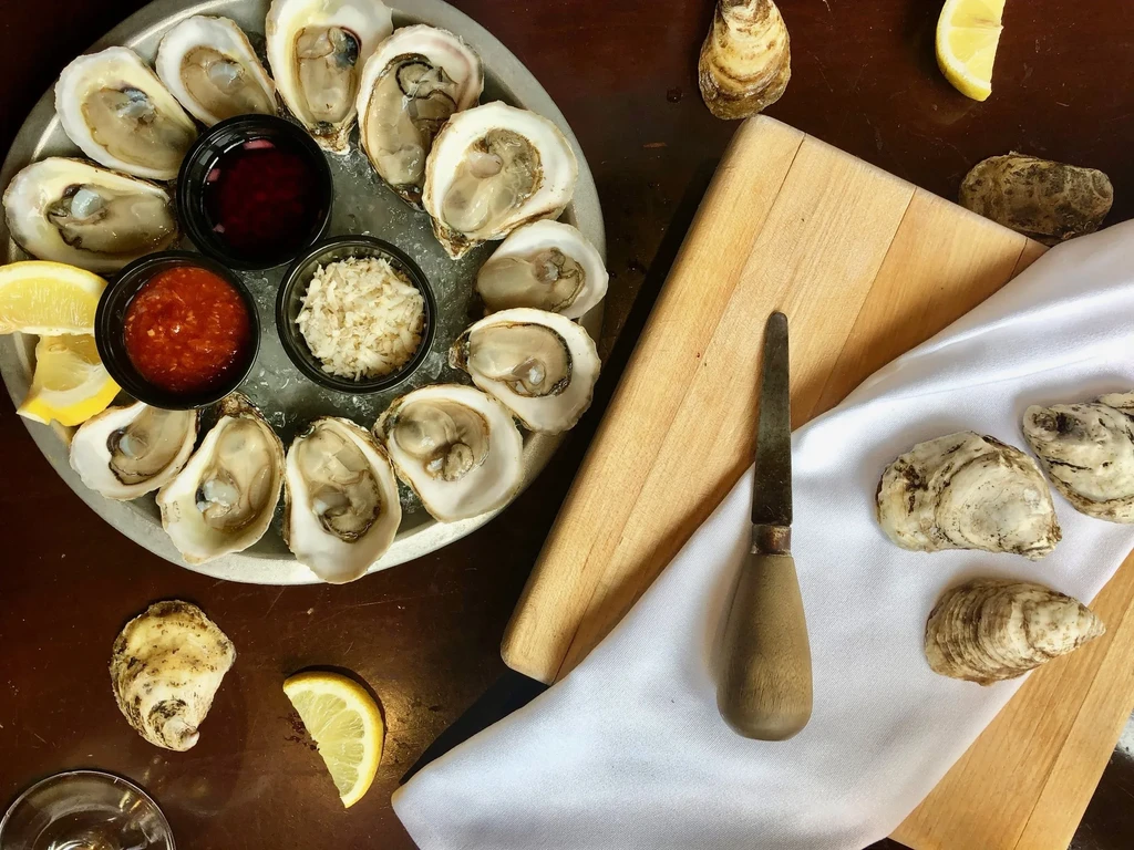 Fresh oysters on half-shell, on ice, with condiments and lemons.