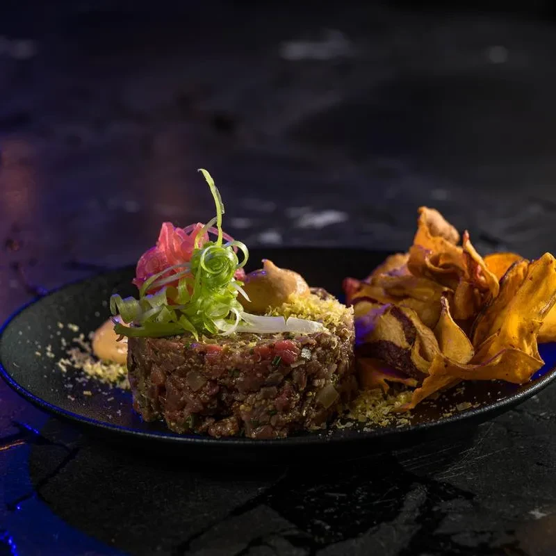 Close-up of garnished meat tartare and colorful root vegetable chips.