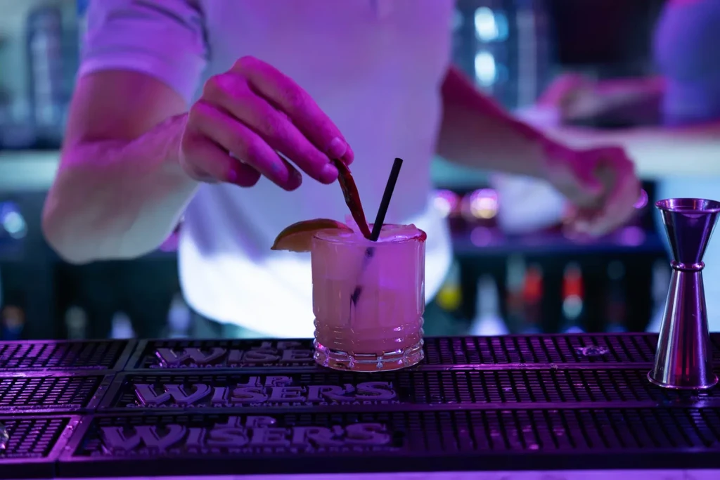 Bartender garnishes a cocktail with lime and a long red garnish.