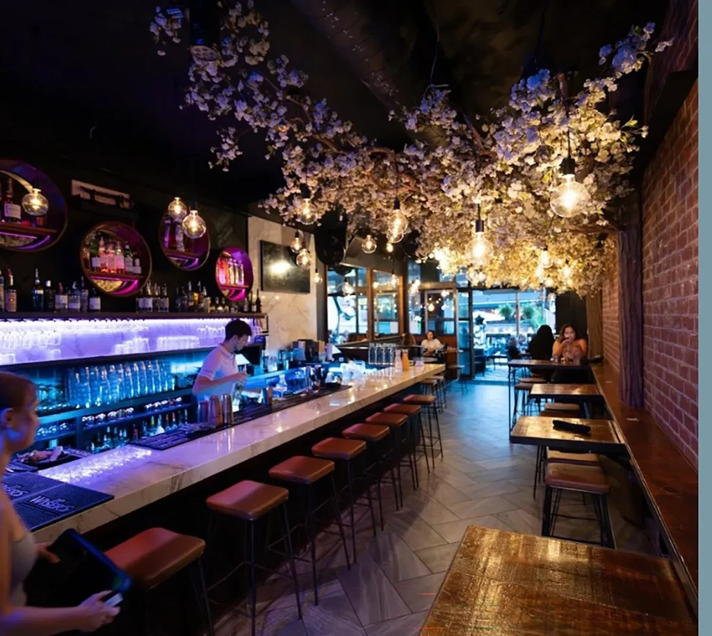 Bar interior: white cherry blossoms, Edison lights, busy bar and patrons.