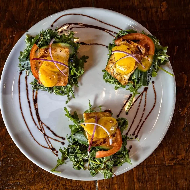 Appetizer: three seared protein portions with greens, yellow sauce, balsamic glaze.