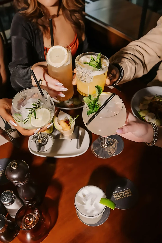 Five elaborately garnished cocktails held by hands in a celebratory toast.
