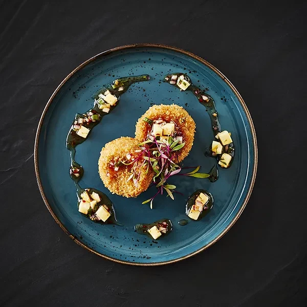 Two breaded patties, microgreens, and dark sauce on a blue-green plate.