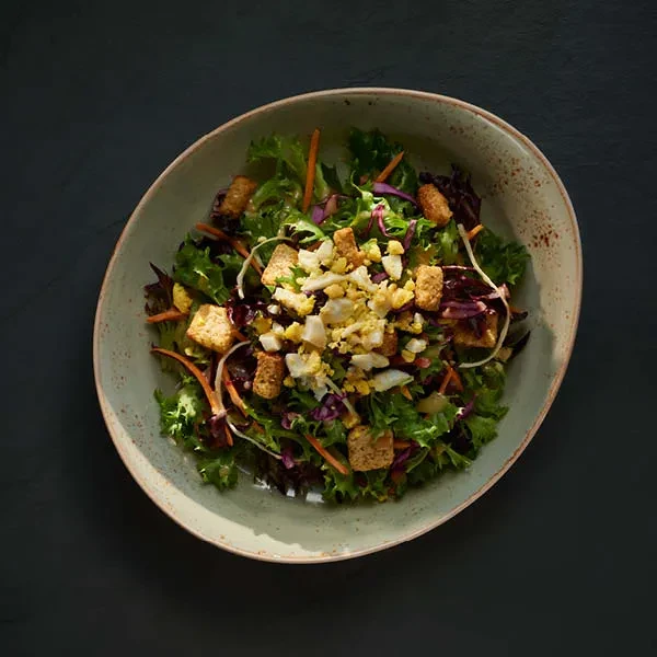 Vibrant salad with mixed greens, carrots, egg, and croutons in a rustic bowl.