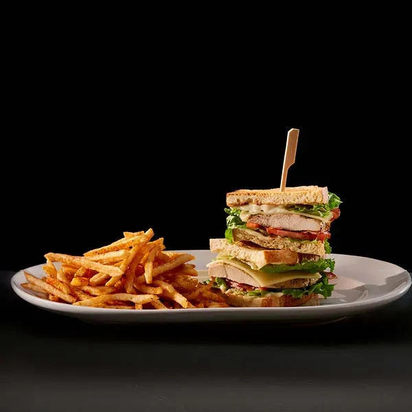 A tall club sandwich and seasoned french fries on a white plate.