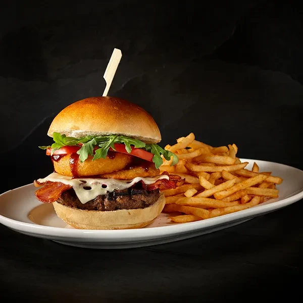Gourmet burger and fries on a white plate, dark background.
