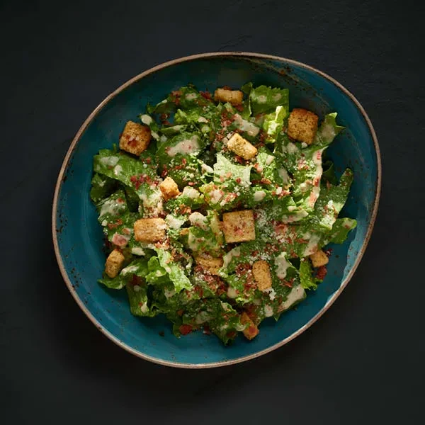 Caesar salad with creamy dressing, croutons, and cheese in blue bowl.