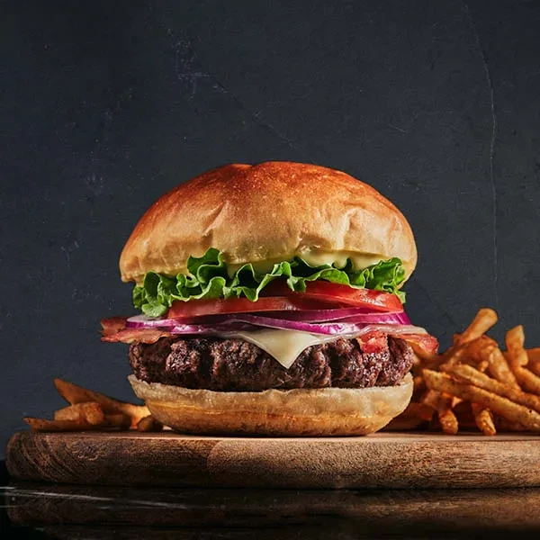 Gourmet burger with melted cheese, bacon, and fries on wood.