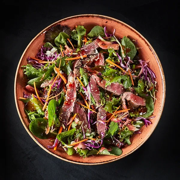 Rustic bowl with vibrant salad, rare meat, vegetables, and sesame seeds.